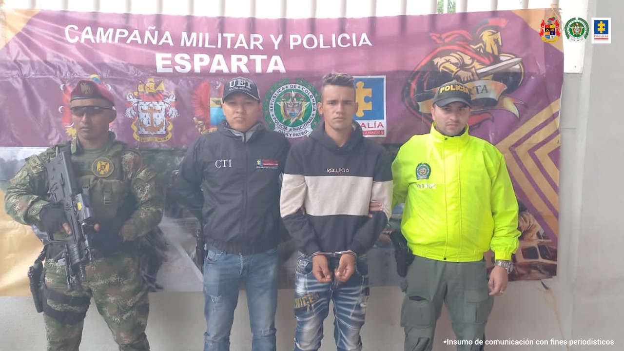 En la fotografía se observan a cuatro personas, una de ellas es el capturado. Los otros tres son integrantes de la Policía y el Ejército Nacional, y un integrante del Cuerpo Técnico de Investigación, adscrito a la Unidad Especial de Investigación. En la parte posterior hay un backing de la campaña militar Esparta con escudos de la Policía, Ejército y la Fiscalía.