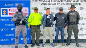 En la fotografía aparece el capturado junto a dos funcionarios del CTI y dos agentes de la Policía Nacional. En la parte superior está un banner de la Fiscalía General y otro banner de la Policía Nacional.