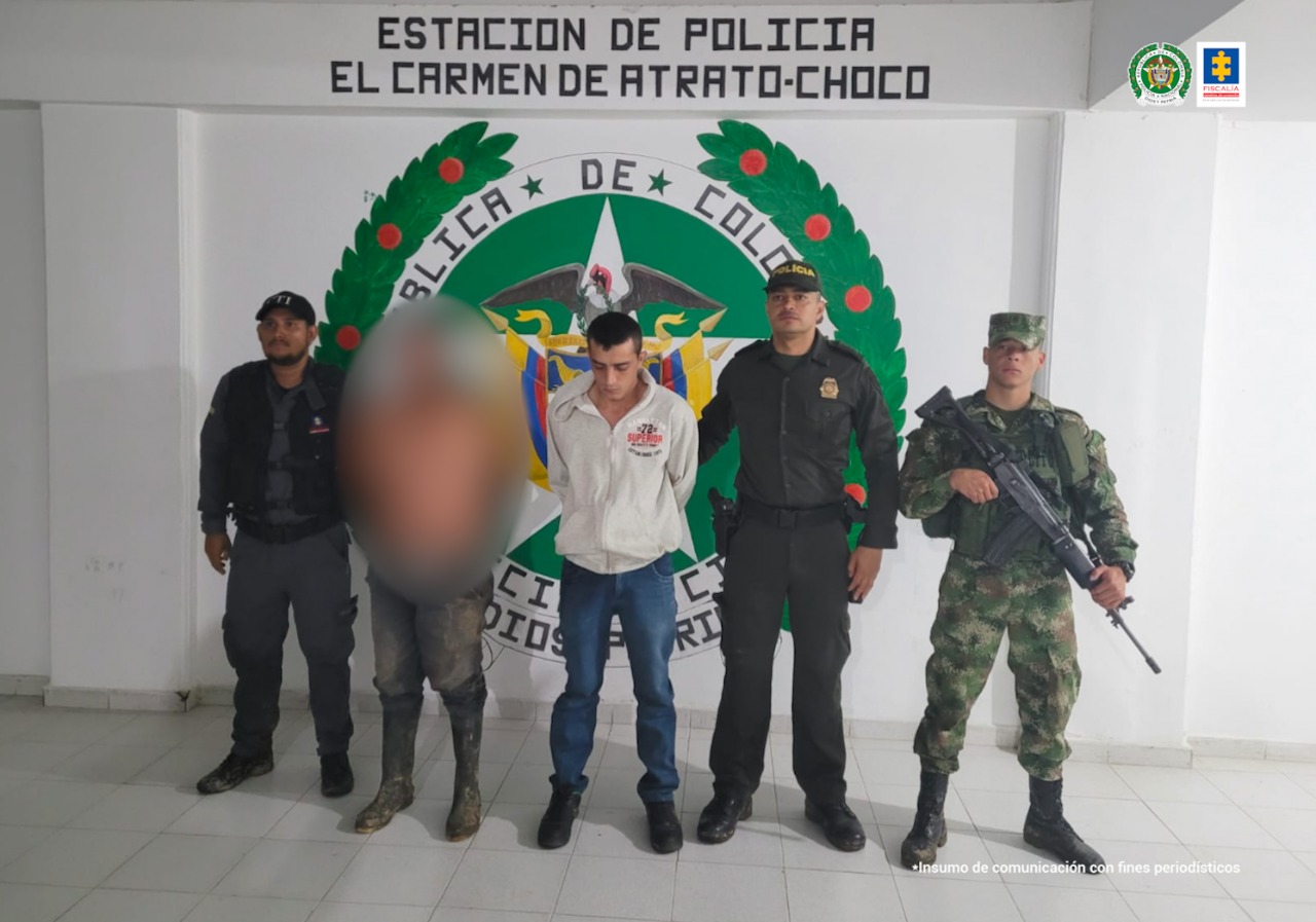 En la fotografía, aparecen dos hombres, uno de ellos pixelado completamente, en el fondo tienen el escudo de la Policía Nacional y el nombre de la Estación de Policía de Carmen de Atrato (Chocó). Tienen a sus lados uniformados del Cuerpo Técnico de Investigación (CTI) de la Fiscalía, La Policía y La Armada Nacional.