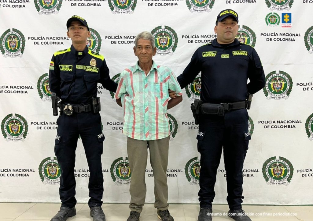 En la imagen aparece una persona de pantalón café y camisa verde, entre dos uniformados de la Policía Nacional.