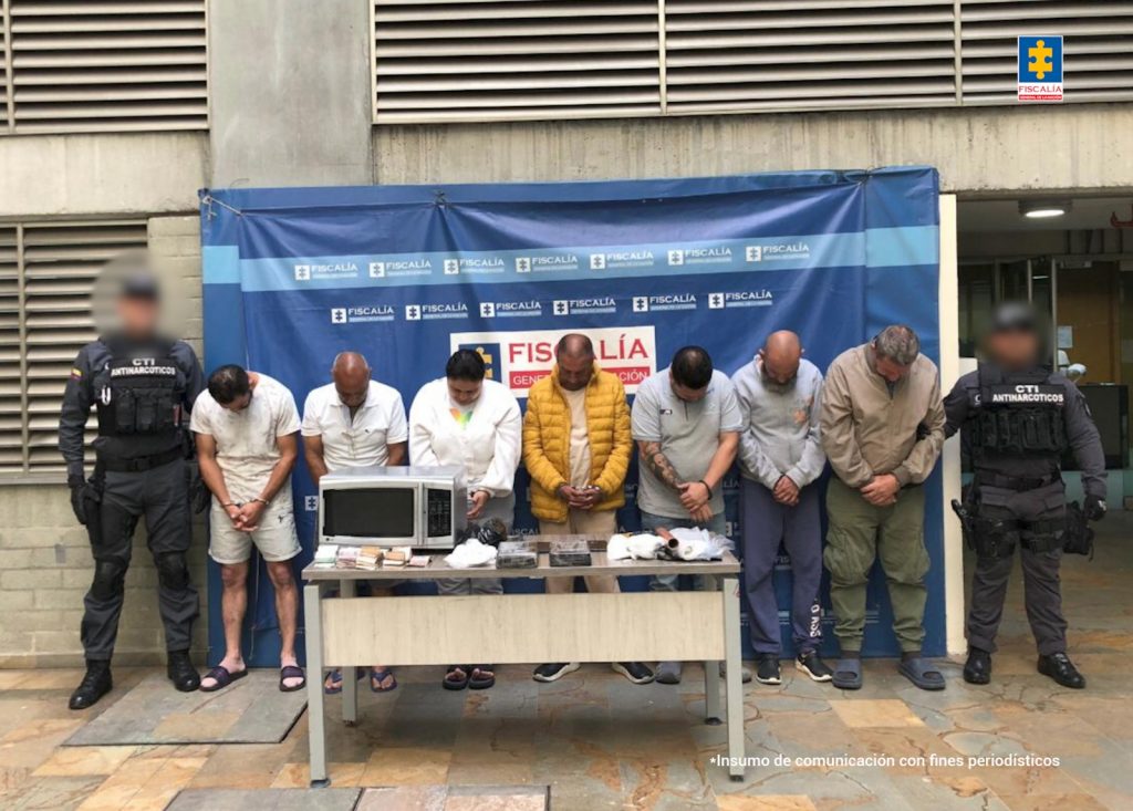 En la fotografía hay 7 procesados en medio de 2 servidores del CTI y una mesa al frente con los elementos incautados