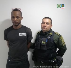 En la fotografía se aprecia de pie y con los brazos atrás a Álvaro Rodríguez Solís. Viste con camiseta y pantalón de color negro. Utiliza lentes como diadema. A su izquierda hay un uniformado de la Policía Nacional.