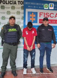 En la imagen se ve una persona detenida bajo custodia de un investigador del CTI y de la Policía. Detrás suyo backings institucionales.