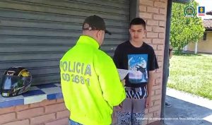 En la foto aparece de pie Anderson Arias Salazar, alias El Mister. Viste camiseta de manga corta negra con estampado de un delfín; asimismo pantalón estampado. Frente a él hay un uniformado de la Policía Nacional quien tiene en sus manos un documento.