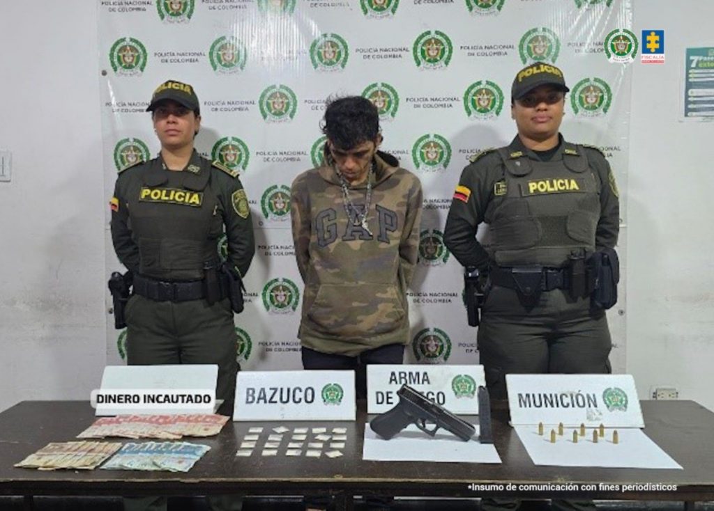 En la fotografía aparece de pie, con los brazos atrás y la cabeza inclinada hacia adelante, Ánderzon Humberto Giraldo Vásquez. Viste con buso camuflado y pantalón oscuro. Usa una cadena en el cuello.  En sus extremos hay uniformados de la Policía Nacional. Delante de ellos hay una superficie marrón y sobre ella hay un arma de fuego, munición y dinero en efectivo. Asimismo, se ven bolsas plásticas pequeñas con contenido blanco. Igualmente  Detrás de ellos hay un pendón institucional de la Policía.