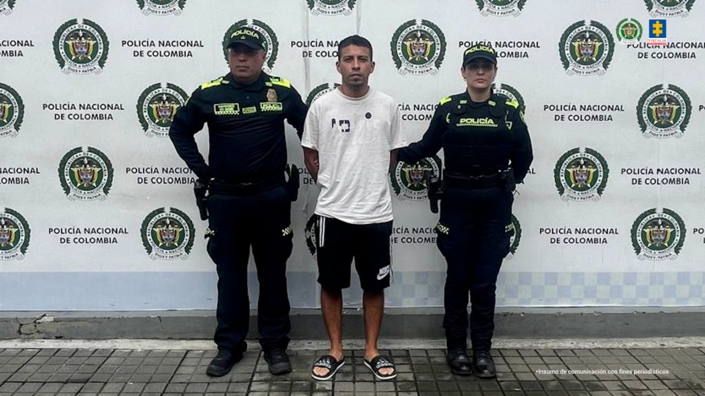 En la fotografía aparece de pie y con los brazos atrás Andinson Kevin Girón Martínez. Viste con camiseta blanca, de mangas cortas, bermuda de color negro y algunos estampados en blanco, así como pantuflas negras. En sus extremos hay uniformados de la Policía Nacional. Detrás de ellos hay un pendón  institucional de la Policía.