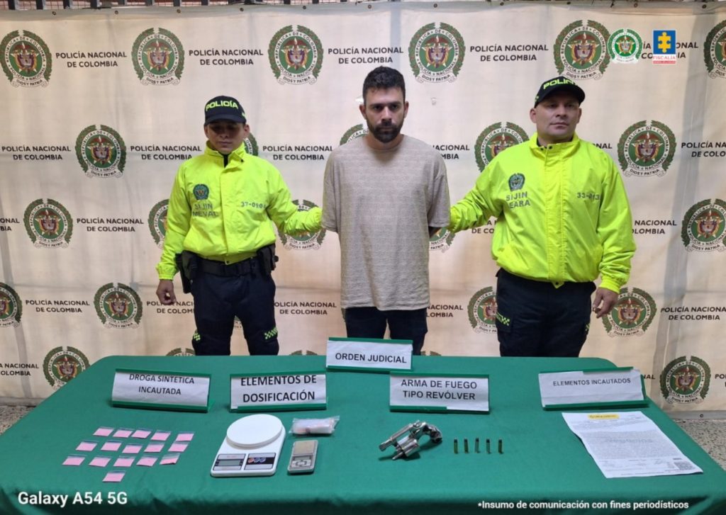 En la imagen está el procesado con dos servidores de la Policía Nacional a los lados y una mesa con los elementos incautados