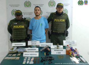 En la fotografía se aprecia de pie y con los brazos atrás Andrés Fernando Muñoz López. Viste camiseta de manga corta azul celeste. A lado y lado de él hay uniformados de la Policía Nacional. Delante de ellos hay una superficie verde y sobre ella varios letreros y elementos alusivos a: ‘Marihuana’, ‘Bolsas Ziploc’, ‘Gramera’, ‘Droga sintética’, ‘Armas de fuego’, ‘Granada de humo’, ‘Munición 9 mm’, ‘Insumos para elaboración de 2CB’. En la parte de atrás hay un pendón institucional de la Policía.