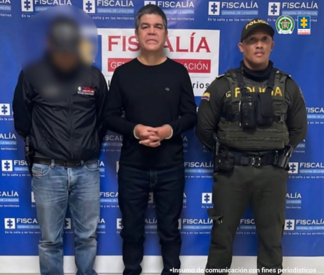 En la fotografía se aprecia a Andrés Gustavo Ricci García, de pie, con los brazos adelante y esposado, el día de su captura. Viste buzo de manga larga, pantalón y zapatos de color negro. Al lado derecho de él hay un servidor del CTI de la Fiscalía y al lado izquierdo de él hay un uniformado de la Policía Nacional. Detrás de ellos hay un pendón institucional de la Fiscalía.
