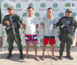 En la fotografía aparecen dos personas capturadas, acompañados de uniformados de la Policía Nacional y el Ejército. En la parte posterior un banner con logos de la entidad.