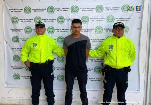 En la imagen aparece una persona de suéter gris y azul entre dos uniformados de la Policía.