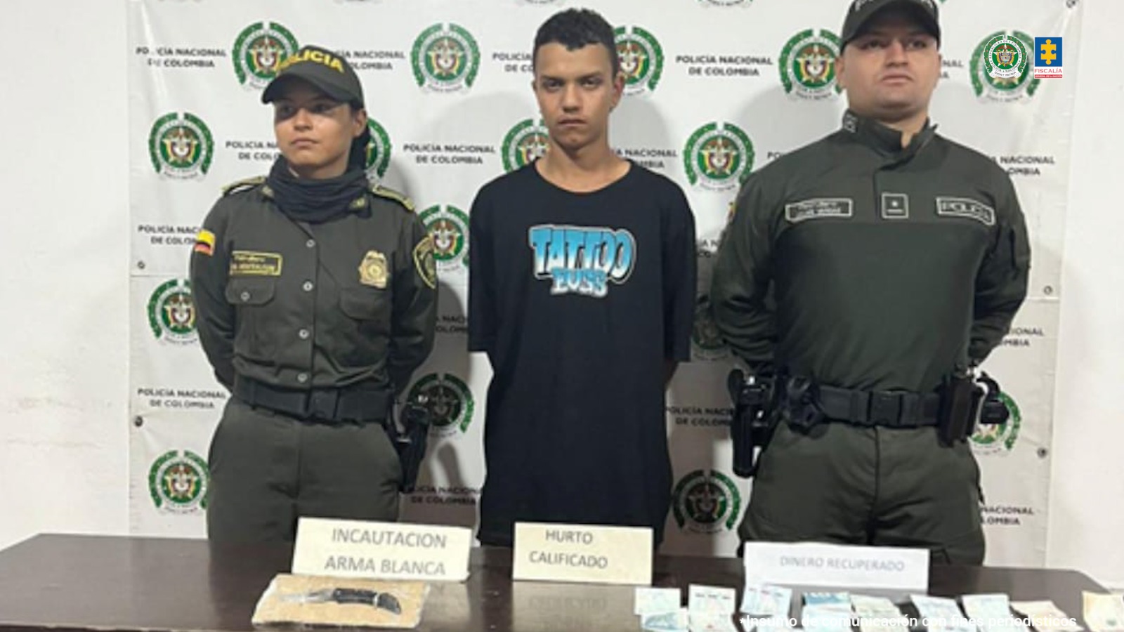 En la Fotografía se aprecia de pie y con los brazos atrás a Angelo Molina González. Viste camiseta de manga corta de color negro con la palabra ‘Totto’ estampada, a la altura del pecho, en azul y blanco. A sus extremos hay uniformados de la Policía Nacional. Delate de ellos hay una superficie de color marrón y sobre ella hay una navaja, dinero en efectivo y tres letreros que dicen: ‘Incautación arma blanca’, ‘Hurto calificado’ y ‘Dinero recuperado’. Detrás de ellos hay un pendón institucional de la Policía.