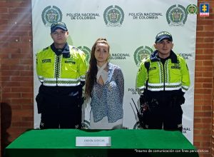 capturada custodiada por dos policías. Detrás banner de la Policía Nacional.