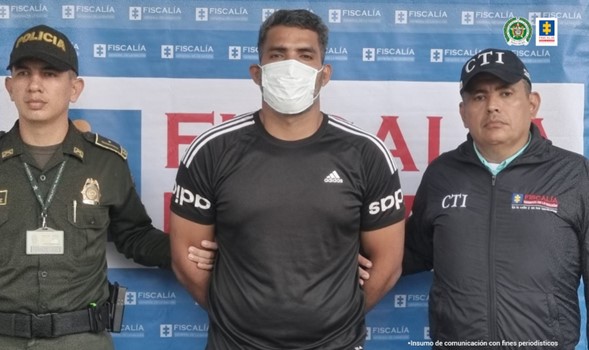 En la imagen aparece el capturado junto a un uniformado de la Policía Nacional y un investigador del CTI. En la parte de atrás se observa el banner de la Fiscalía General de la Nación.