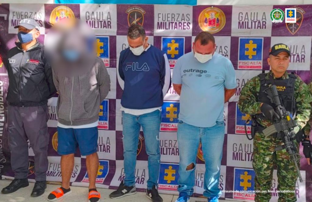 En la fotografía están los capturados con las manos en la espalda, esposados y uniformados de la Policía Nacional los custodian. Está además el backing con el logo oficial de esta institución y del Ejército Nacional.