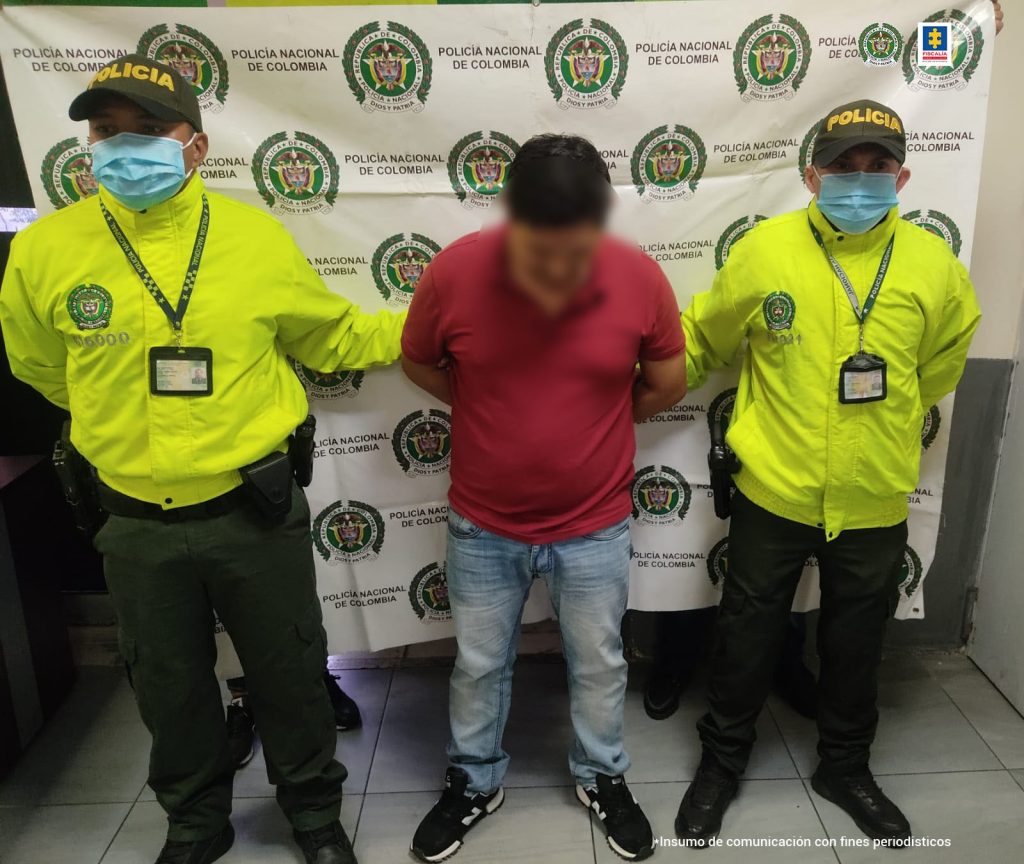 En la imagen se ve al procesado con una camisa roja, esposado y custodiado por dos uniformados de la Policía Nacional, tras su captura en Puerto Colombia.