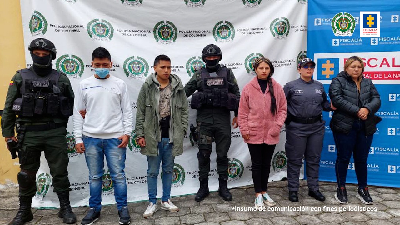 En la fotografía aparecen 4 de los 5 presuntos miembros de la banda Dulces Sueños junto a un funcionario del CTI y un agente del GOES de la Policía Nacional. En la parte posterior se ve un banner de la Fiscalía General y otro banner de la Policía Nacional. 