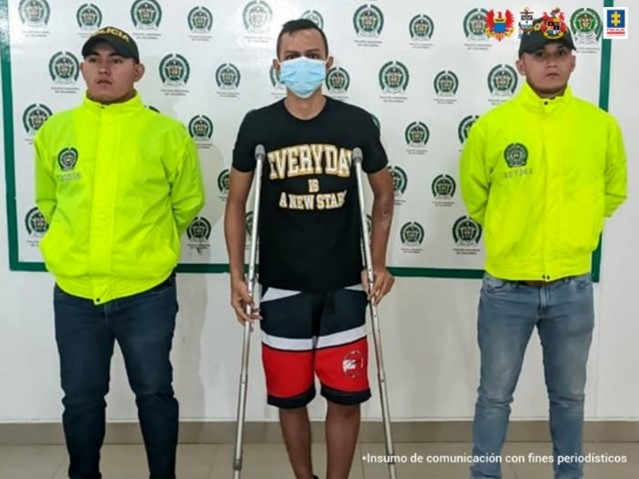 En la imagen se aprecia el capturado en muletas, junto a dos uniformados de la Policía Nacional, en la parte posterior se observa el banner de la Policía Nacional.