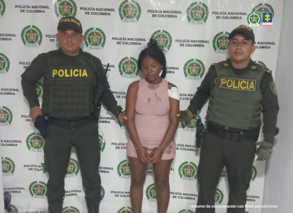 En la imagen aparece una mujer de vestido color rosa entre dos uniformados de la Policía Nacional.