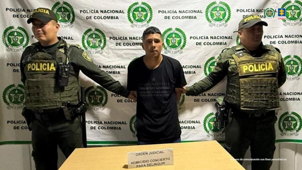 En la fotografía aparece de pie y con los brazos atrás Brandon Estiven Foronda Ríos. Viste con camiseta de mangas cortas, de color negro. A sus extremos hay uniformados de la Policía Nacional. Delante de ellos hay una superficie y sobre ella hay un letrero que dice: ‘Orden judicial homicidio concierto para delinquir’. Detrás de ellos hay un pendón institucional de la Policía, sede Sevilla (Valle del Cauca).
