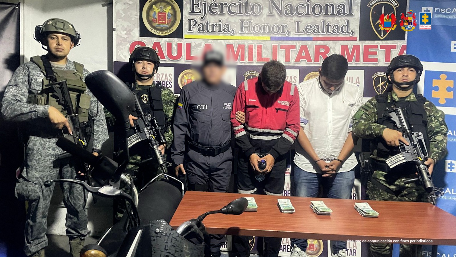 capturados de frente custodiados por investigador del CTI de la Fiscalía y militares de Ejército y Fuerza Aérea colombiana. Detrás banner de Fiscalía y Gaula Militar.