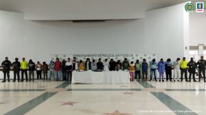 En la imagen están las 21 personas capturadas, con servidores de la Policía Nacional custodiándolos.