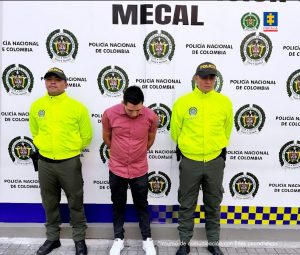 El procesado se encuentra esposado y en custodia por un uniformados de la Policía Nacional. Detrás suyo un backing de la Policía.