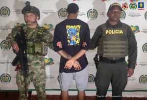 En la imagen aparece el investigado, de espaldas, y en medio de un soldado y un patrullero de la policía.