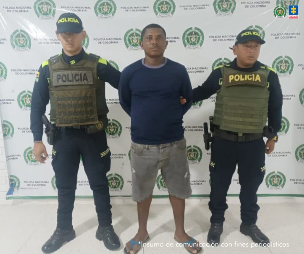 En la imagen aparece una persona de suéter azul y bermuda de jean entre dos uniformados de la Policía Nacional. 