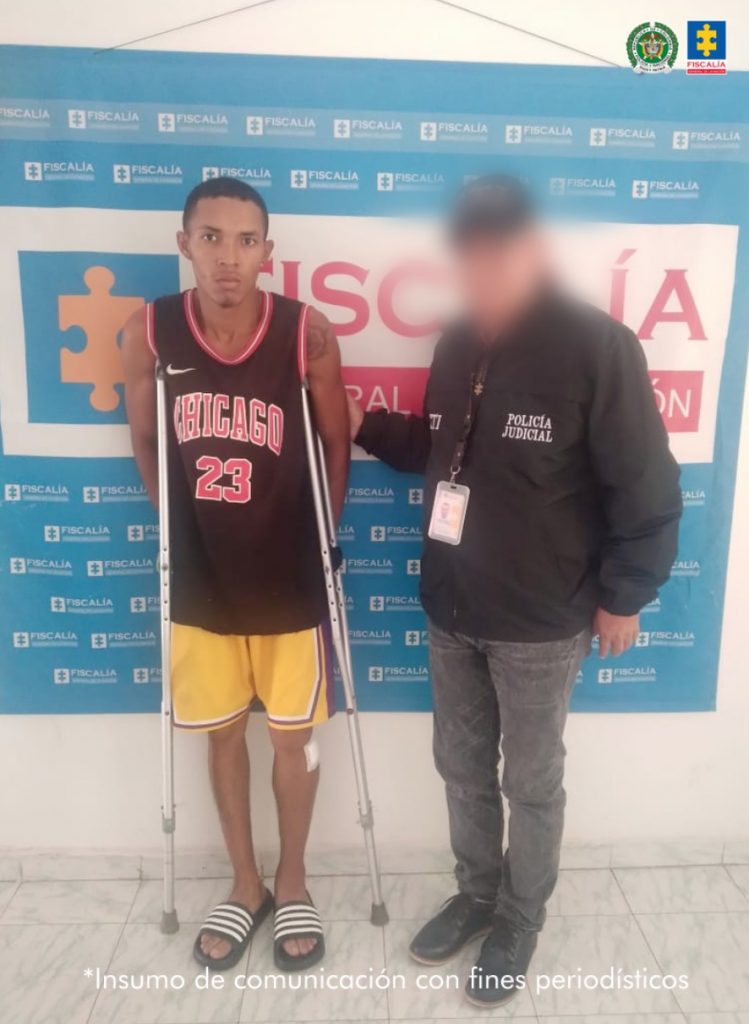 En la imagen aparece una persona de bermuda amarilla y camiseta deportiva negra, junto con un uniformado de la Policía. 