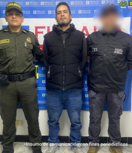 En la fotografía aparece el capturado junto a un funcionario del CTI y un uniformado de la Policía Nacional. En la parte superior está un banner de la Fiscalía General.