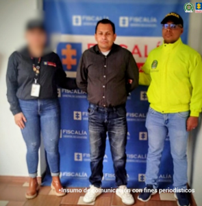En la fotografía aparece el capturado junto a una servidora del CTI y un uniformado de la Policía. En la foto en la parte superior está un banner de la Fiscalía.