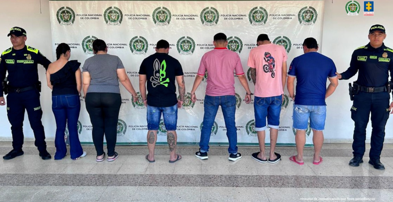 En la foto aparece los capturados custodiados por dos uniformados de la Policía Nacional.  En la foto también aparece de fondo un backing de la Policía Nacional.