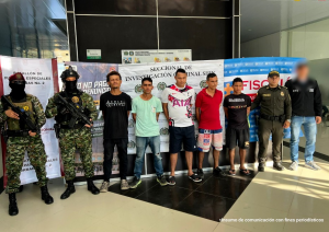 Se visualiza a los capturados junto a un investigador del CTI y uniformados de la Policía y Ejército Nacional. Detrás de ellos los banners que identifican a la Fiscalía, Policía y Ejército Nacional.