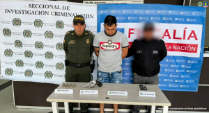 Se visualiza al capturado junto a un uniformado de la Policía Nacional y un investigador del CTI.  Frente a ellos una mesa con los elementos incautados como: revólver, munición y un teléfono celular. Detrás de ellos los banners que identifican a la Policía Nacional y Fiscalía General de la Nación.