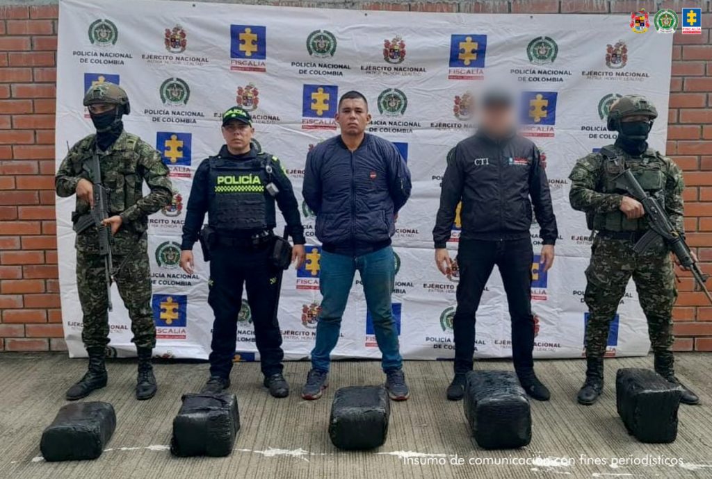 El capturado se encuentra de frente y custodiado por un servidor del Cuerpo Técnico de Investigación CTI, un uniformado del Ejército y la Policía Nacional. Detrás se observa un backing de la Policía y Ejército Nacional. Así mismo, se ven los paquetes del estupefaciente.