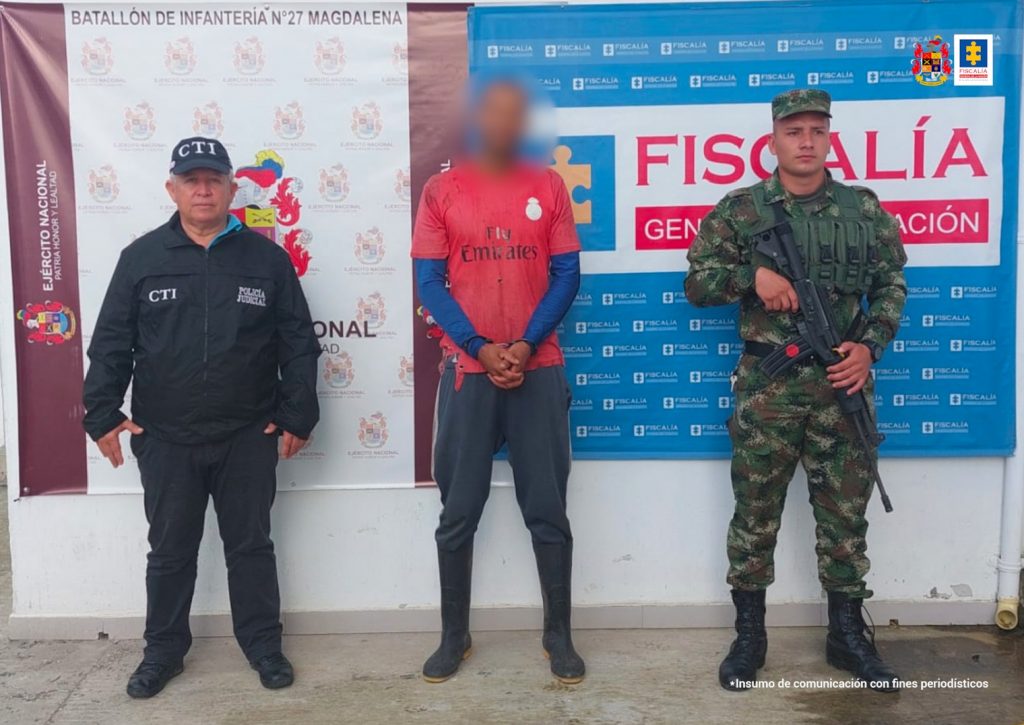 En la fotografía aparece un capturado junto a personal de Fiscalía General de La Nación y Ejército Nacional. En la parte posterior de la imagen se ven banners de Ejército Nacional y la Fiscalía General de la Nación.