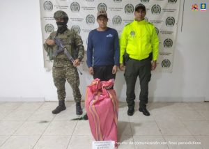  En la foto aparece el capturado custodiado por un uniformado del Ejército y Policía Nacional. De fondo aparece un backing de la Policía Nacional. En la foto aparece el costal que le incautaron al procesado con el permanganato y manganato de potasio.