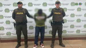 Capturado es imputado por la Fiscalía por delitos sexuales. Texto Alternativo: capturado de frente custodiado por dos policías. Detrás banner de la Policía Nacional.