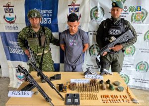 En la fotografía aparece le capturado junto a un infante de la Armada Nacional y un uniformado de la Policía Nacional. En la parte posterior, está una mesa con armas, munición, explosivos, detonadores eléctricos, entre otros elementos.