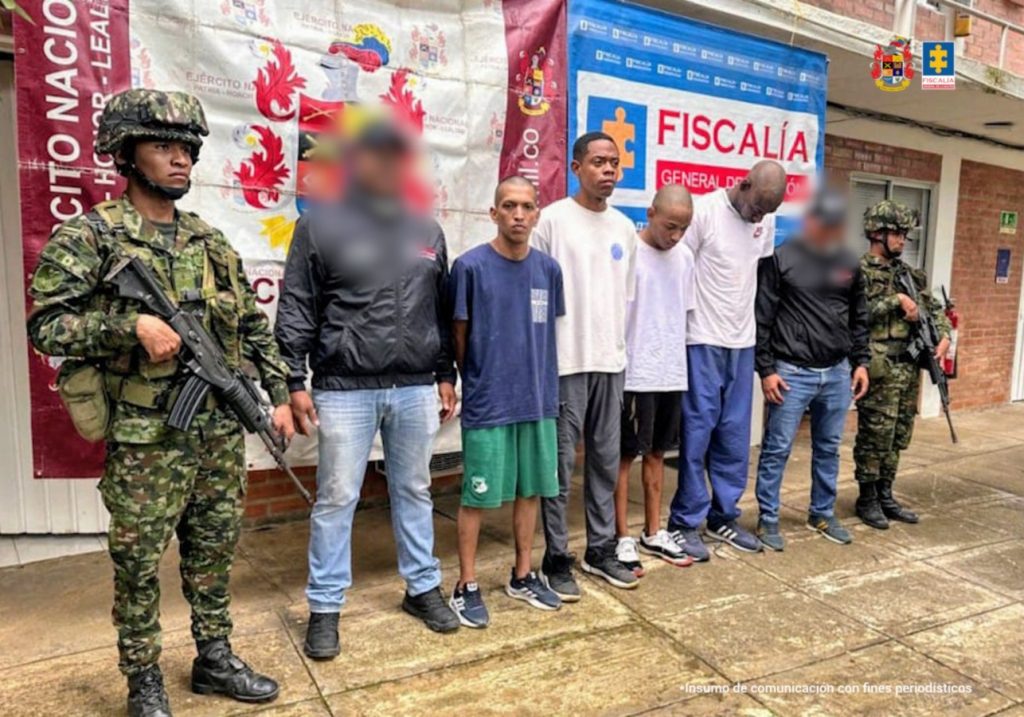 En la fotografía aparecen los cuatro capturados junto a dos funcionarios del CTI y dos soldados del Ejército Nacional. En la parte superior están un banner de la Fiscalía General y un banner del Ejército Nacional.