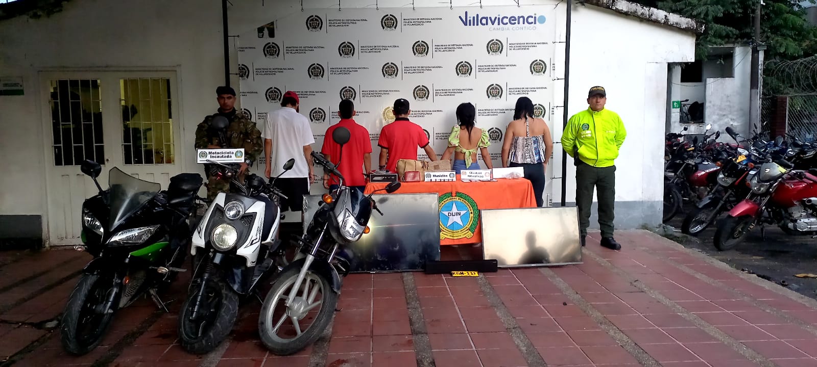 En la foto están los tres capturados de frente custodiados por dos uniformados de la Policía y dos militares del Ejército Nacional, detrás de ellos los banner de las dos instituciones y delante de ellos una mesa con el material incautado en las diligencias.