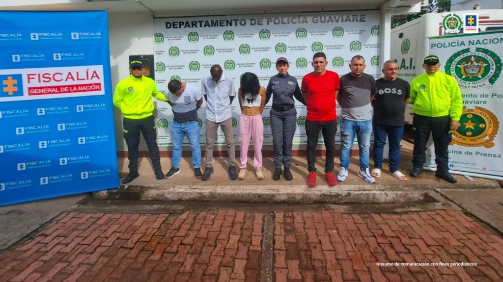 capturados de frente custodiados por policías. Detrás banner de Policía y Fiscalía.