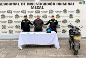 En  la fotografía aparec de pie y con los brazos atrás Carlos Alberto Arango García. Viste con camiseta de color negro y estampado blanco en lado izquierdo del pecho. En sus extremos hay uniformados de la Policía Nacional. Delante de ellos hay una mesa, con mantel blanco y sobre ella se aprecian dos teléfonos celulares y un casco de motociclista. En el extremo izquierdo de la mesa hay una motocicleta. En la parte posterior, hay un pendón institucional de la Policía.