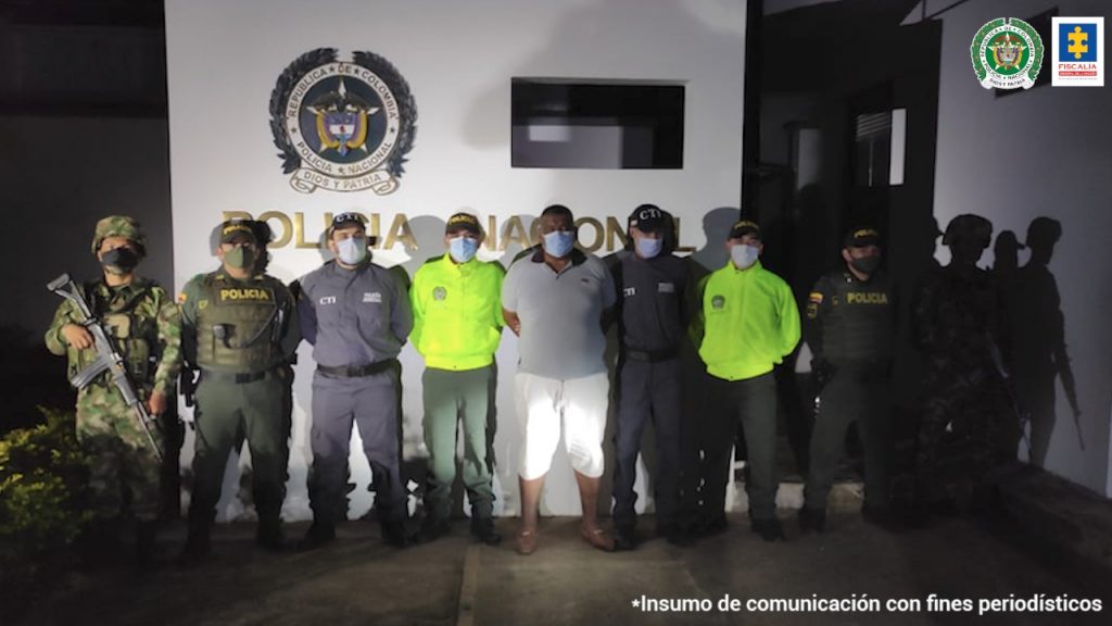 En la fotografía aparece un capturado, junto a personal de Fiscalía General de La Nación, Policía Nacional y Ejército Nacional. En la parte posterior de la imagen se ven banners de Ejército Nacional, Policía Nacional y la Fiscalía General de la Nación.