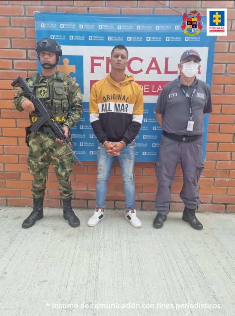 En la fotografía aparece un capturado, junto a personal de Fiscalía General de la Nación y Ejercito Nacional. En la parte posterior de la imagen se ven banners de Ejército Nacional y la Fiscalía General de la Nación.