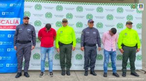 En la imagen se ven dos personas detenidas bajo custodia de integrantes de la Policía Nacional y el CTI. Detrás suyo backings institucionales.