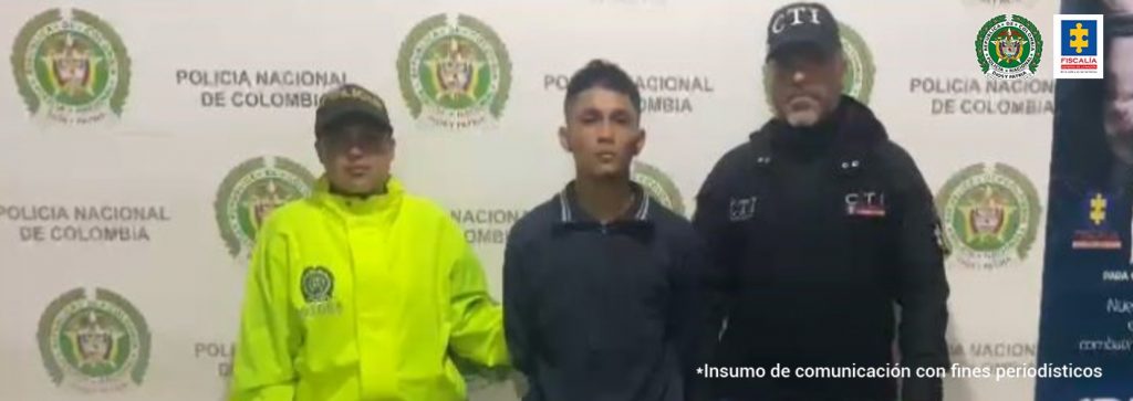 En la foto aparece de pie y con los brazos atrás Carlos Andrés Ortega Yanguatín, alias Tanga. Viste camiseta oscura, de manga corta y cuello; jean con diferentes desgastes. Al lado derecho de él hay una uniformada de la Policía Nacional y al lado izquierdo un servidor del CTI de la Fiscalía. Detrás de ellos se aprecian dos pendones institucionales de la Policía y de la Fiscalía.