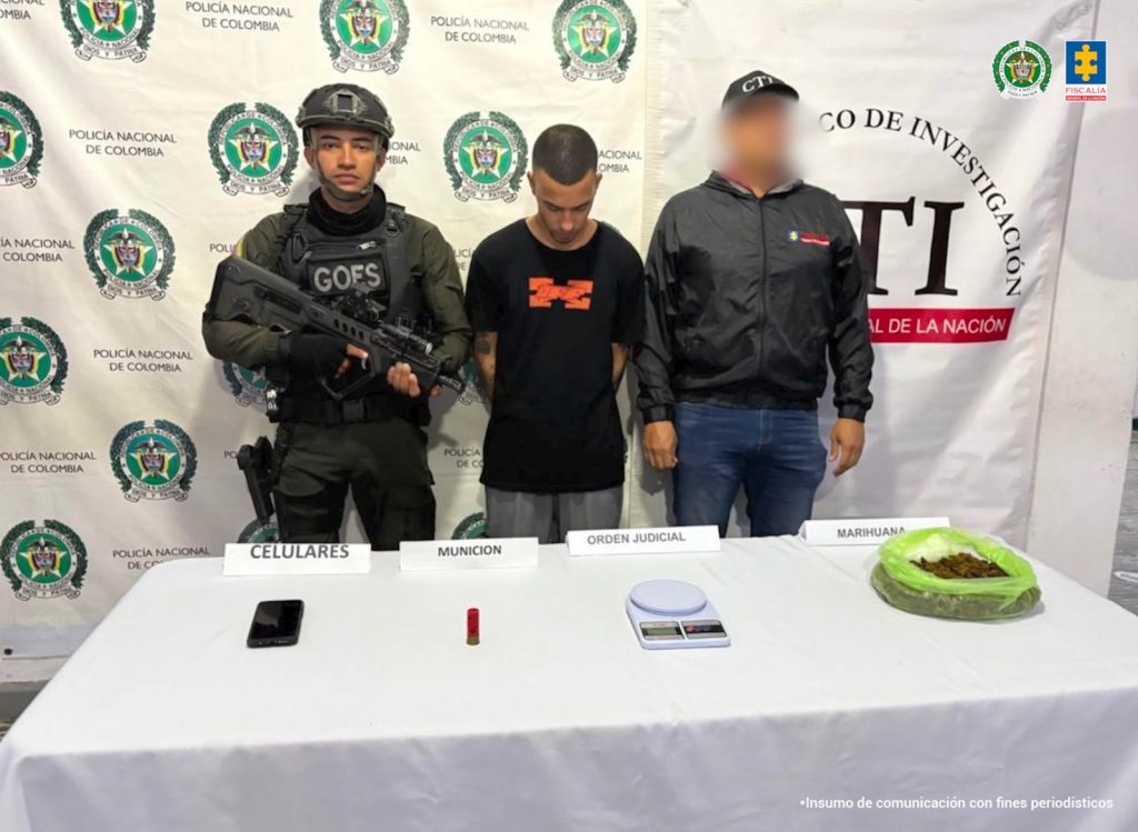 En la fotografía aparece de pie, con la cabeza inclinada hacia adelante y los brazos atrás Carlos Armando Ramírez López. Viste con camiseta de color negro y logo de color rojo a la altura del pecho; así como pantalón de color gris. En su extremo izquierdo hay un servidor del CTI de la Fiscalía y en el derecho hay un uniformado de la Policía Nacional. Delante de ellos hay una superficie blanca y sobre ella se ve un celular, un  cartucho, una gramera y una bolsa plástica de color verede con contenido vegetal. Detrás de ellos hay dos pendones institucionales de la Fiscalía y Policía.