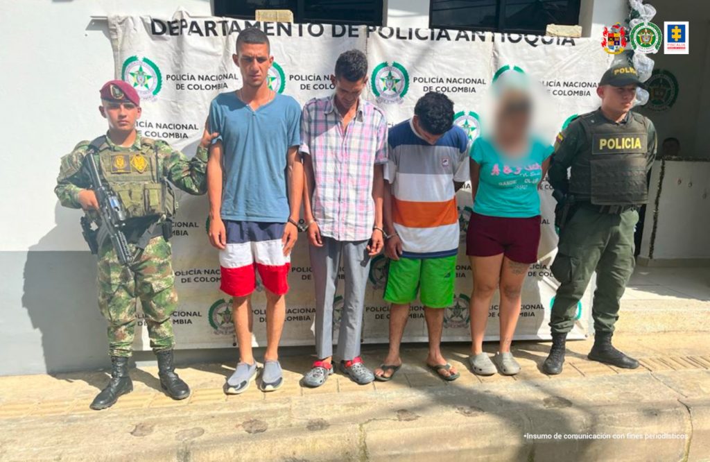 En la fotografía están los 3 procesados esposados con un pendón de la Policía Nacional y servidores del Ejército y la Policía a los lados